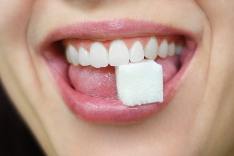 Closeup of a women's mouth with a sugar cube between her teeth