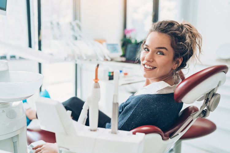 Brunette woman smiles in a dental chair awaiting recovery tips after root canal therapy