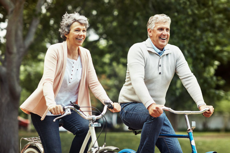 A husband and wife with snap-on dentures and dental implants smile as they ride bikes together