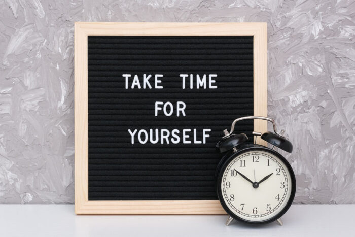 Letter board that says "Take Time for Yourself" next to a clock and a gray wall