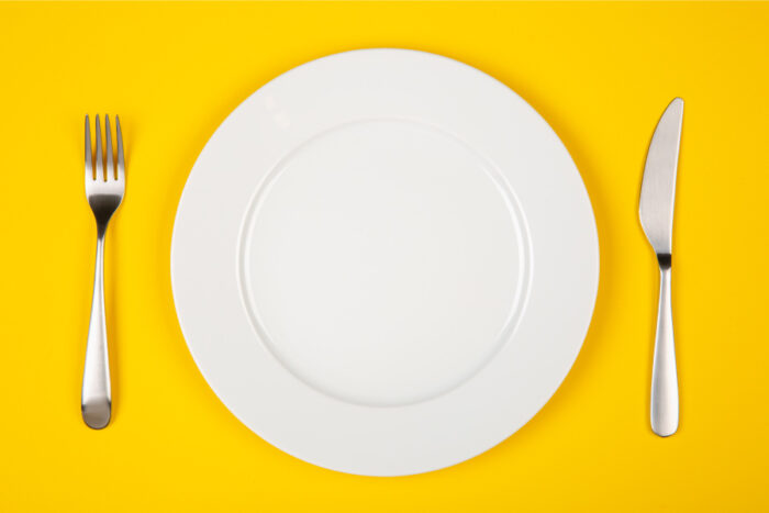 Aerial view of a white plate and silverware against a yellow table