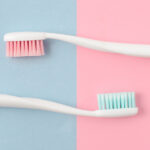 A white toothbrush with blue bristles and a white toothbrush with pink bristles against a blue and purple background
